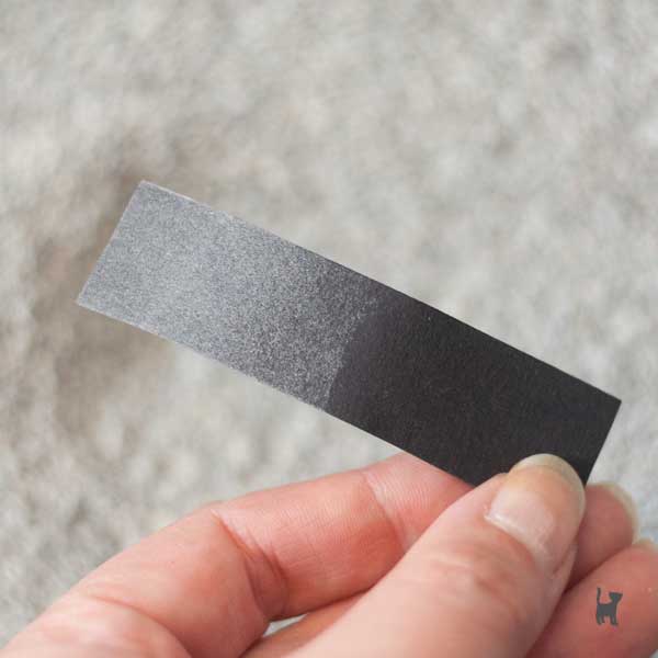 Schwarzer Pappstreifen mit viel grauem Staub auf einer Hälfte